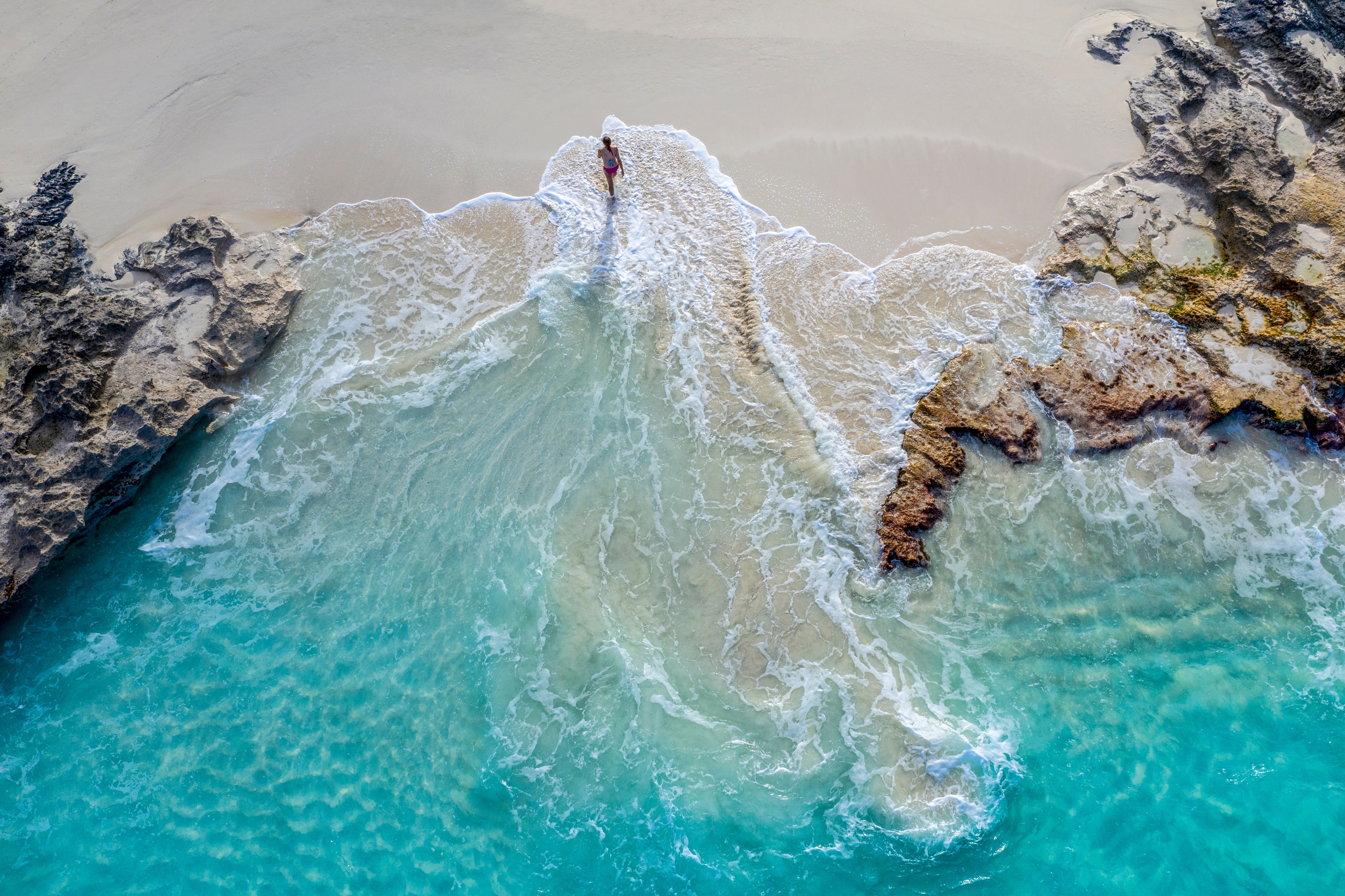 An aerial view of a person running on a white-sand Caribbean beach in Exuma, Bahamas 