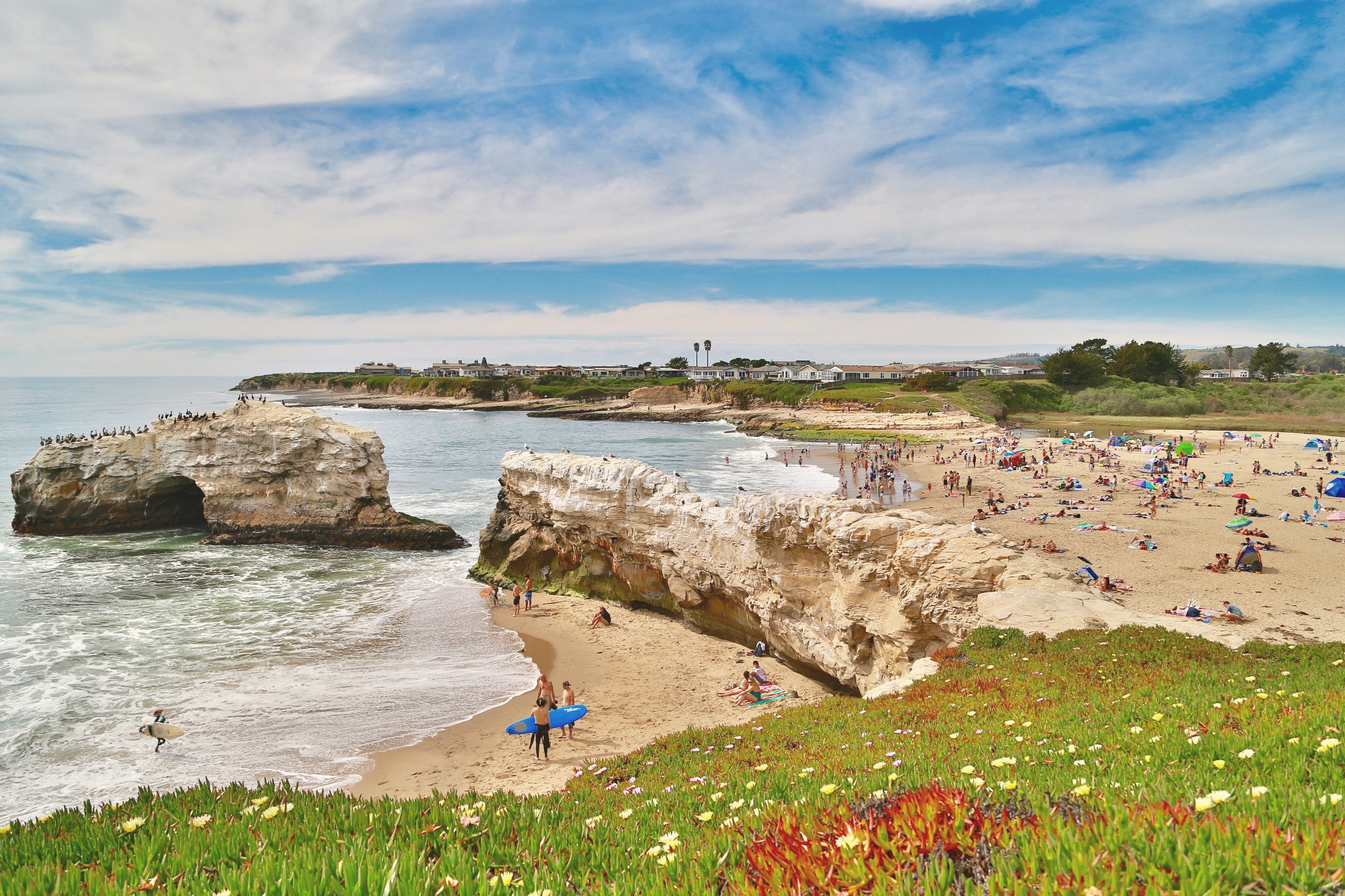 Sunbathers and surfers on a large beach with rocky outcrops in Santa Cruz, California 